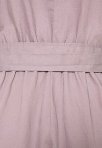 Tissu rose clair avec une finition douce et texturée. Tissu froncé sous une ceinture horizontale, créant une silhouette fluide et structurée.