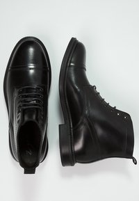 Černé kožené boty s hladkým povrchem, šněrováním, kulatou špičkou a plochou gumovou podrážkou. Obsahují ševové detaily a kovové očka.