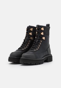 Botas de combate de cuero negro con punta redonda, suela gruesa, detalles de hardware dorado, diseño de cordones y forro de textil suave.