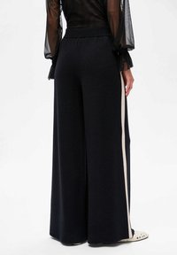 Zwarte wijduitlopende broek van stof, met een crèmekleurige verticale streep aan de zijkant en een gestructureerde afwerking. Elastische tailleband voor comfort.