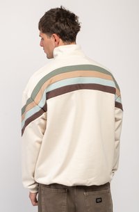 Felpa crema con colletto alto, caratterizzata da righe orizzontali in verde, beige, azzurro chiaro e marrone sulla schiena. Texture liscia.