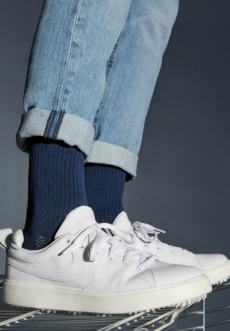 Sneakers bianchi in pelle con una suola in gomma spessa, indossati con jeans in denim azzurro arrotolati e calze in cotone blu navy a coste.