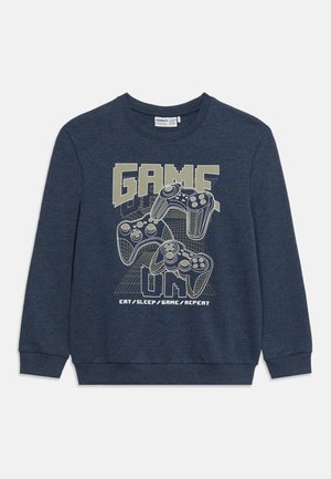 Sudadera azul oscuro con tres mandos de videojuegos contorneados y texto "GAME ON" y "EAT / SLEEP / GAME / REPEAT" en el frente.