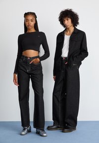 Black ribbed crop top, high-waisted black jeans with white stitching, loose fit, and contrasting pockets. Accessories include metallic shoes.
