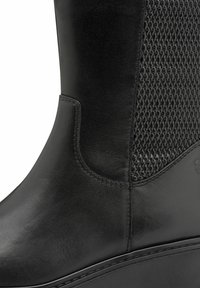 Fekete bőr bokacsizma texturált hálós betéttel, sima felülettel és kerek orral, amelyen varrott díszítések találhatók a talpon.