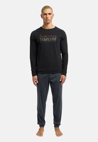 Sort langærmet top med "bruno banani" logo, der er parret med grå joggingbukser, begge lavet af blødt stof. Modellen er barfodet.