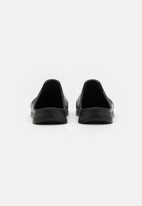 Sapatos pretos de slip-on com um exterior liso, traseira arredondada e sola texturizada com um padrão zigzag. Sem costuras ou enfeites visíveis.
