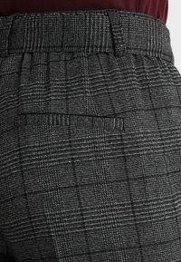 Grå rutiga byxor med en texturerad tyg. Har en midjeresår och en bakficka. Mönstret inkluderar tunna och tjocka linjer i svart och grått.