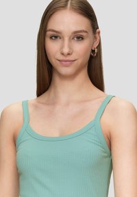 Hellgrünes, geripptes Tanktop mit dünnen Trägern, das eine figurnahe Passform und eine glatte Textur aufweist. Keine auffälligen Muster oder Hardware-Details.