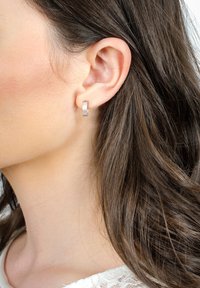 Silverörhängen med texturerad yta, cirkulär form och släta kanter, båda båda på vänster öra. Håret faller ner över axeln.