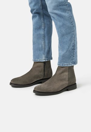 Botines de ante gris con punta redonda, cierre de cremallera y suela de goma negra, combinados con unos pantalones vaqueros de mezclilla azul claro.