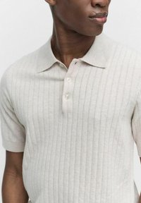 Ljusbeige kortärmad polo tröja gjord av texturerad stickad tyg, med subtila vertikala ränder och en tre-knapplåsstängning.