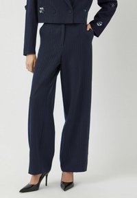 Granatowe szerokie spodnie w paski wykonane z gładkiego materiału, z wysokim stanem i kieszeniami, w zestawieniu z czarnymi czółenkami na szpilkach.