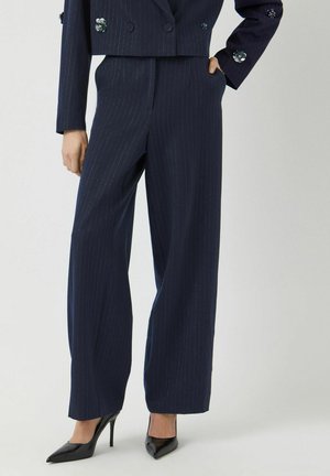 Marineblauwe, gestreepte, wijde broek gemaakt van een gladde stof, met een hoge taille en zakken, gecombineerd met zwarte, puntige hakken.
