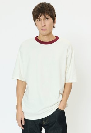 Tricou alb din bumbac cu guler rotund burgund, mâneci scurte, croială lejeră, asortat cu pantaloni din denim închis. Design minimalist.