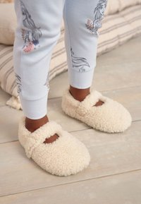 Chaussons duveteux couleur crème avec une surface douce et texturée et un design à bride Mary Jane. Confort chaud et douillet, idéal pour l'intérieur.