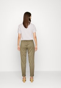Camisa cinza-claro de mangas curtas, combinada com calças verdes-oliva ajustadas. O conjunto apresenta um corte casual com punhos dobrados e saltos de madeira.