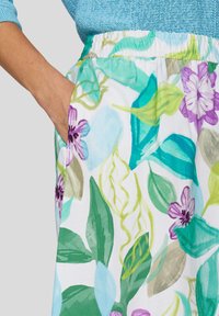 Floral-patterned skirt featuring green leaves and purple flowers, made of light fabric with an elastic waistband and side pockets.