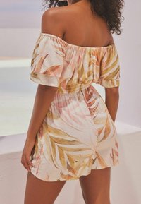 Romper sans épaules en tissu léger, avec un imprimé de feuilles rose et doré, une taille smockée et des manches courtes.