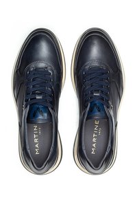 Mornarske kožne tenisice s glatkom površinom, okruglim vrhom, bijelim đonom i plavim vezicama. Unutrašnjost sadrži naziv i logotip marke.