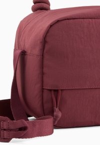 Borsa a tracolla in tessuto bordeaux con forma rettangolare, superficie testurizzata, tracolla regolabile e un piccolo dettaglio con tasca elastica.