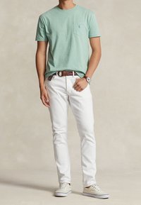 Mintgrön t-shirt med kort ärm och bröstficka, vita jeans, brun bälte och beige sneakers. Silverklocka på handleden; färgglad randig midja.