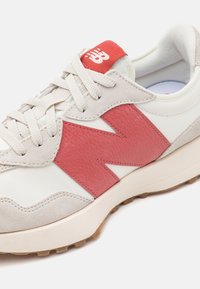 Weiß-beige Sneakers mit rotem Leder "N"-Logo an der Seite, beigen Schnürsenkeln, rotem Etikett auf der Zunge und gepolsterter Sohle mit strukturiertem Boden.