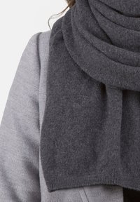 Šedý pletený šátek vyrobený z jemného materiálu, s robustním designem a rovnoměrnou texturou, posazený kolem krku, doplňující šedý oděv.