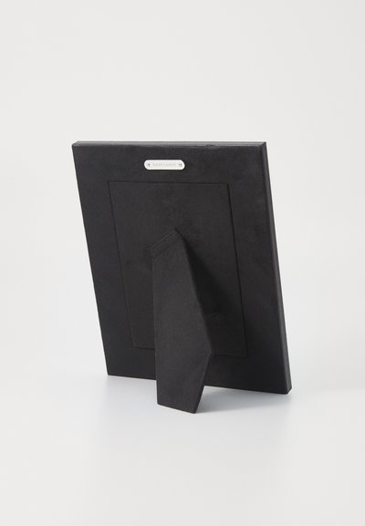 Svart fotoramme med teksturert overflate, utstyrt med en støtte og en liten sølvfarged logoplate på baksiden. Enkel rektangulær design.