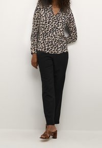 Blusa leggera con stampa leopardata, maniche lunghe e scollatura a V, abbinata a pantaloni neri su misura e sandali con tacco marroni.