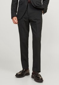 Svarta skräddarsydda kostymbyxor, slim fit, slät front, sidofickor, tillverkade av slät tyg. Utsmyckad med en subtil lyster. Kombineras med mörka loafers.