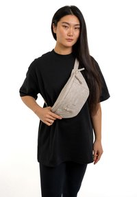 Marsupio fanny pack beige con motivo geometrico, realizzato in materiale leggero, dotato di chiusura con zip e tracolla regolabile, indossato a tracolla.