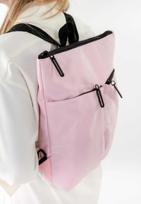Mochila rosa hecha de tela texturizada con cremalleras y herrajes negros. Cuenta con dos bolsillos frontales y correas ajustables.