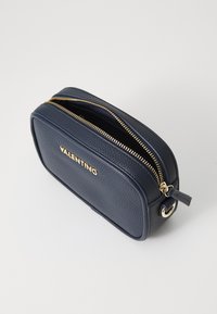 Navy textured leather cosmetic bag with gold zippers and branding, rectangular shape, and a small pull tab on the zipper.
