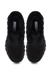 Zapatos negros sin cordones con un forro suave y peludo y una suela de goma resistente. Presentan una parte delantera redondeada y un detalle de costura en contraste.