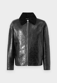 Veste en cuir noir avec une finition brillante et texturée. Elle dispose d'un col en fourrure noire, d'une fermeture éclair à l'avant et de poches latérales.