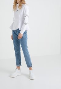 Felpa bianca con peplum e dettagli del logo sulle maniche, abbinata a jeans chiari a gamba affusolata e sneaker bianche chunky. Tessuto morbido, vestibilità casual.