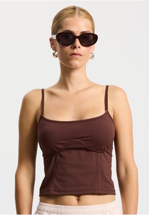 Brun cropped tanktop med tynde stropper, rynkede detaljer og glat tekstur. Kombineret med mørke solbriller og øreringe i ring.