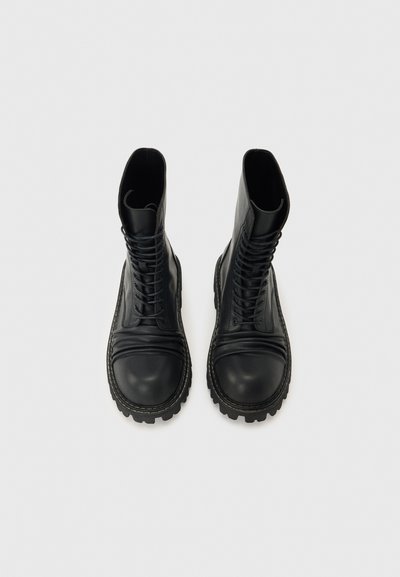 Ζευγάρι μαύρα δερμάτινα στρατιωτικά μποτάκια με κορδόνια και παχιά, ανθεκτική σόλα, φωτογραφημένα από επάνω με φόντο απλή επιφάνεια.