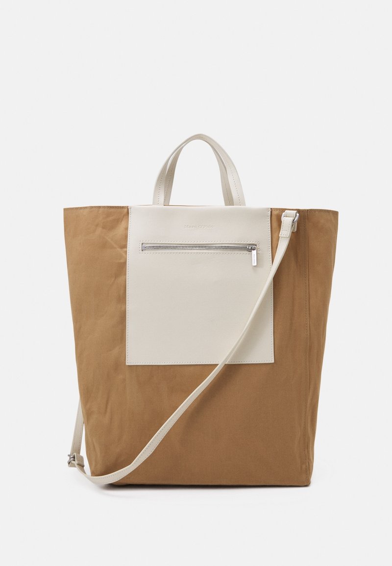 Sac cabas marron avec grande poche avant blanche zippée, poignées courtes et longue bandoulière blanche réglable sur fond uni.