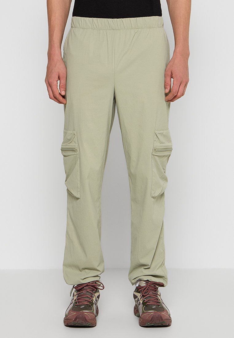 Helle khaki Cargo-Hosen mit elastischem Bund, zwei Seitentaschen und einer lockeren Passform. Das Material wirkt leicht und strukturiert.