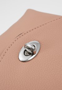 Primo piano di una borsa in pelle color rosa beige con un doppio punto di chiusura ovale in argento e cuciture visibili lungo il bordo.