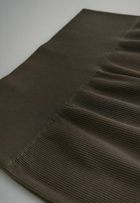 Sötétbarna szövet, amely függőleges bordázott textúrával rendelkezik, finom hajtásokkal az egyik szél mentén, hullámszerű mintázatot alkotva.