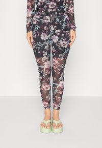 Leggings com estampado floral em tecido preto translúcido, apresentando flores em roxo, azul e rosa, complementadas por sandálias de plataforma verde-claro.