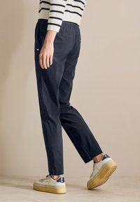 Marineblaue Hose mit entspannter Passform, elastischem Bund und zwei Gesäßtaschen, kombiniert mit weißen Turnschuhen mit marineblauen Akzenten.