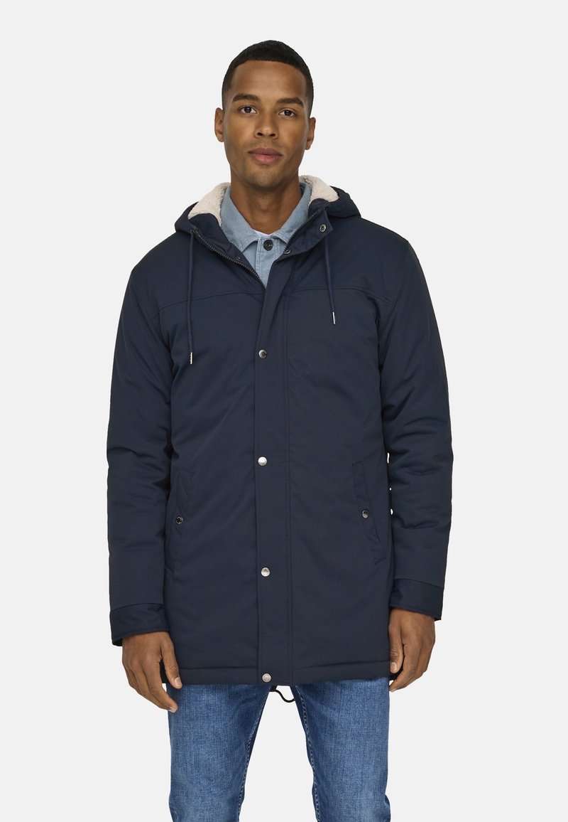 Mörkblå, isolerad parka med justerbar huva, knapp- och dragkedjestängning samt sidofickor. Fodrad med ljusfärgad faux päls.