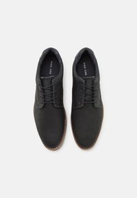 Chaussures noires en cuir perforé avec un bout arrondi, semelle marron contrastante et design à lacets. L'intérieur présente une semelle de marque.