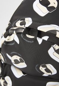 Black fabric backpack featuring repeated graphic designs of a stylized head with sunglasses, accented with "KARL LAGERFELD" text.