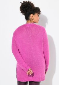 Pull à manches longues en maille ouverte de couleur rose vif. Doté d'un col rond, de poignets côtelés et d'entailles sur les côtés à l'ourlet pour plus de liberté de mouvement.