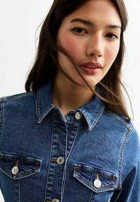Mörkblå denimskjorta med knäppning framtill, kragdesign, två bröstfickor, silverdetaljer och kontrasterande sömnadsdetaljer.